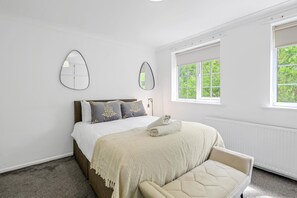 Ein Schlafzimmer mit einem Bett, einer Bank, zwei Spiegeln und einem Fenster mit Blick auf Grünflächen.