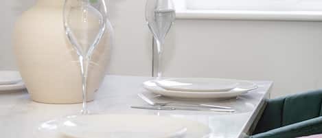 A table set with white plates, a clear glass, and a vase with white flowers.