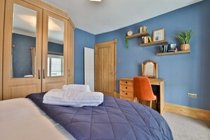 Un dormitorio con una cama grande, un armario de madera, un escritorio con silla y una estantería con libros y una planta.