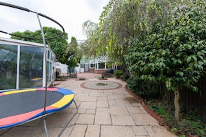 Patio trasero con un trampolín, un porche cubierto y una siega densa.