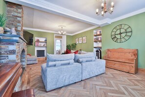 Una sala de estar con piso de espiga, un sofá gris, un mueble de madera y un reloj de pared grande.