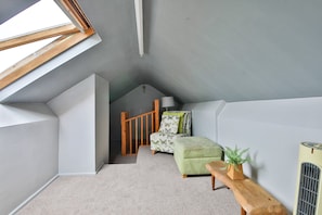 A small, sloped room with a skylight, a wooden bench, a green upholstered bench, and a radiator. - The Swansea Homestay | Spacious 4-Bed Retreat (Swansea)