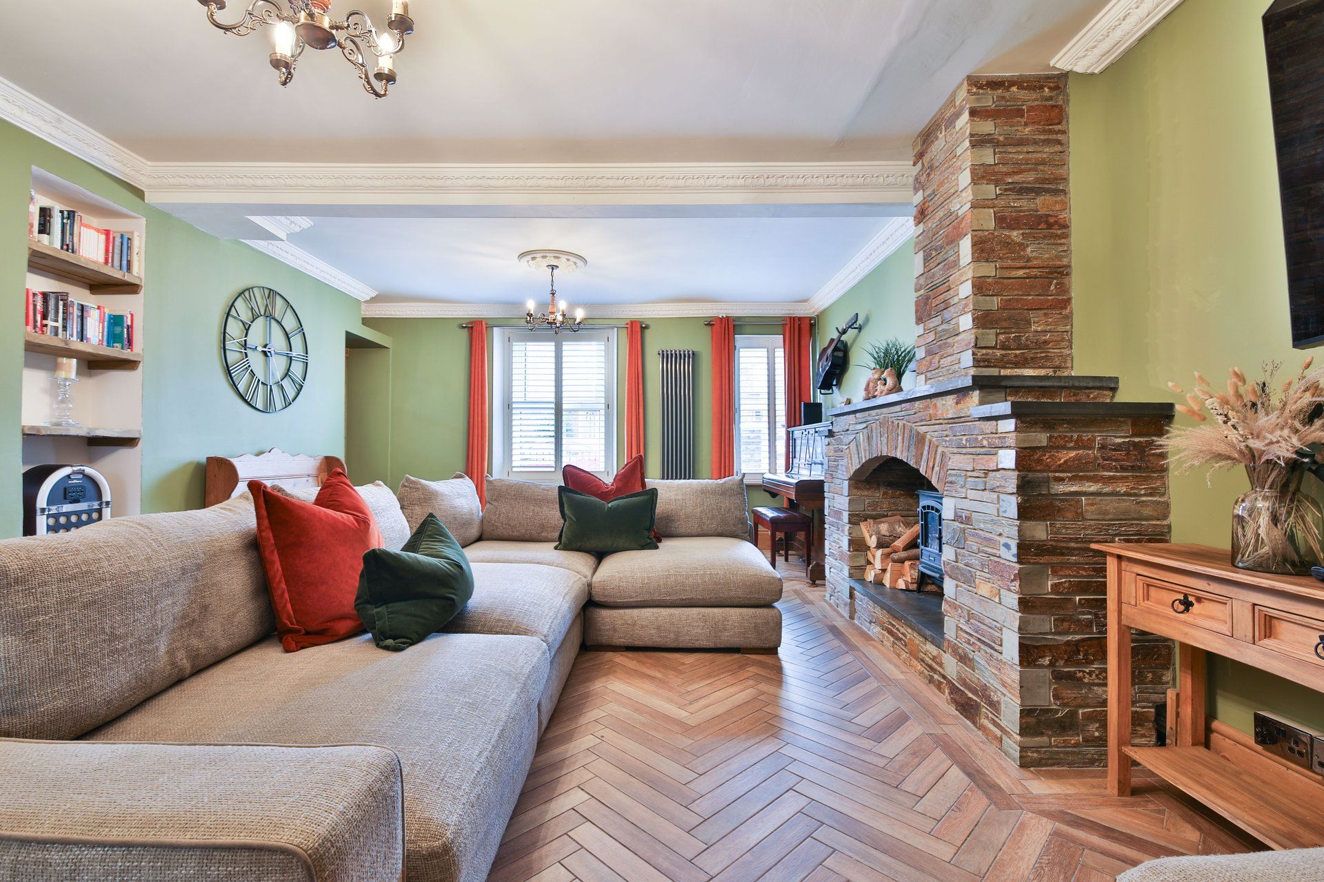 A living room with a herringbone floor, a stone fireplace, a sofa set, and a bookshelf.