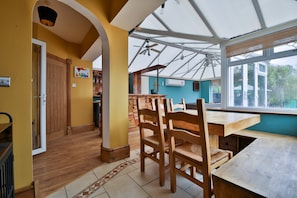 Una habitación con una mesa y sillas de madera, una cocina con armarios de madera y un ventanal con vistas a zonas verdes.