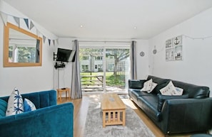 A living room with a blue sofa, a black leather sofa, a wooden coffee table, and a TV on a stand. - Atlantic Reach – Cosy 2-Bed with Parking (Newquay)
