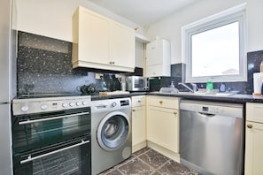 A compact kitchen with an oven, microwave, washing machine, and dishwasher. - Swansea Waterfront 1 Bed Apt with Parking (Swansea)