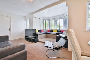 A modern living room with a flat-screen TV, a seating area with a sofa and a bench, and a window with blinds. - Swansea Waterfront 1 Bed Apt with Parking (Swansea)