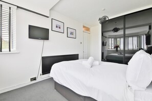 A hotel room with a bed, a TV, and a large window with blinds. - Swansea Waterfront 1 Bed Apt with Parking (Swansea)