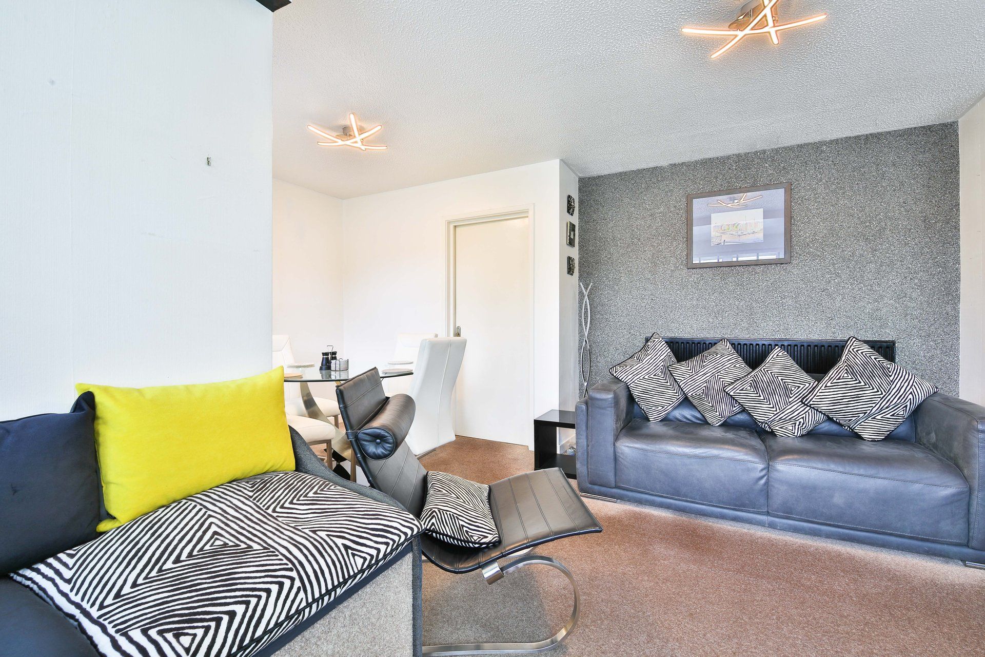 A modern living room with a sofa, a chair, and a coffee table. There is a grey textured wall and a framed picture above the sofa.