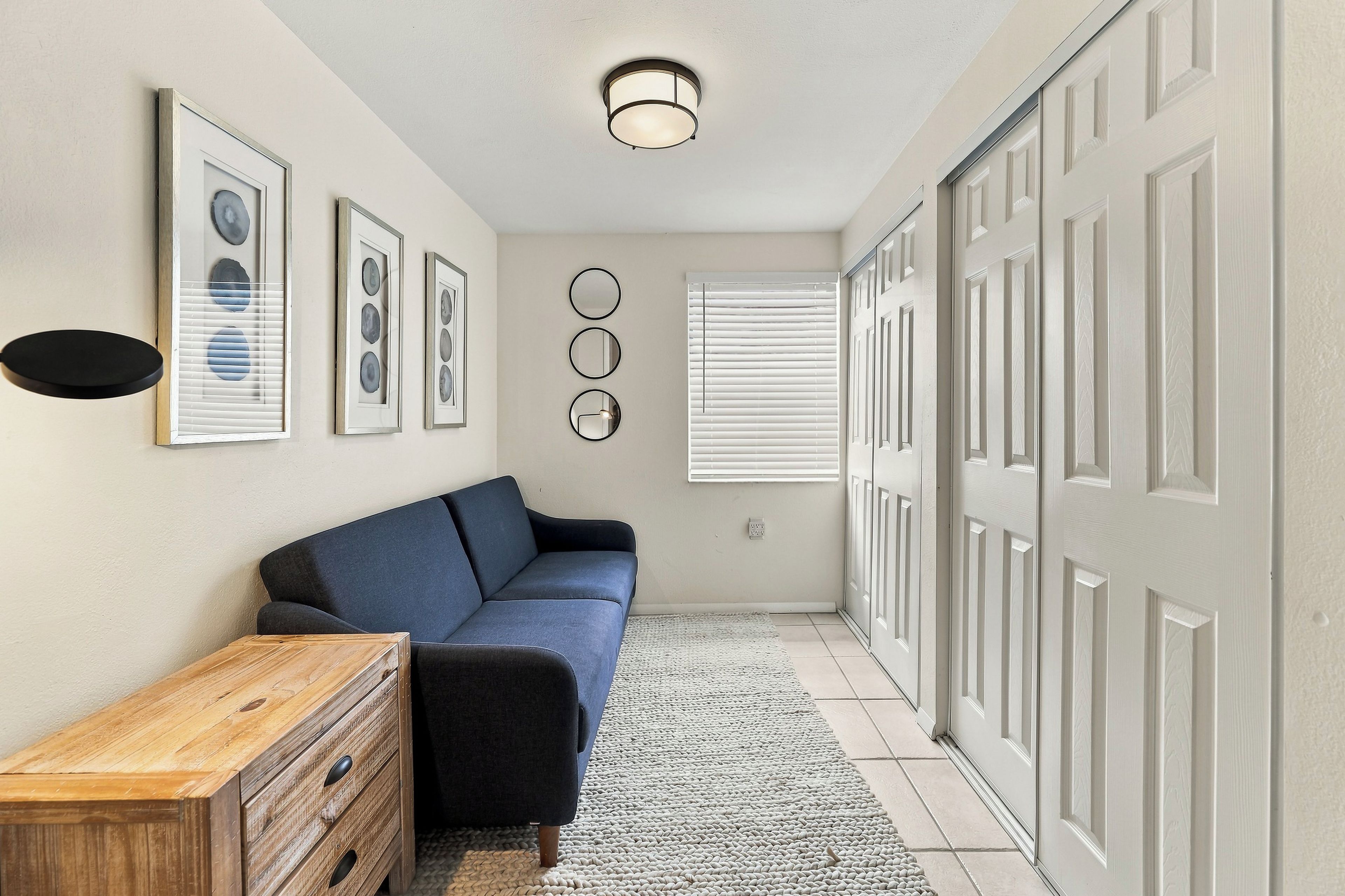 A hallway with a blue sofa, a wooden dresser, framed artwork, a ceiling light, and a door with a window.