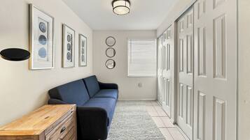 A hallway with a blue sofa, a wooden dresser, framed artwork, a ceiling light, and a door with a window.