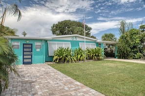 A turquoise building with a flag, a brick pathway, and tropical plants. - Walk to Cocoa Beach + Kids Clubhouse+Private Yard (Cocoa Beach)