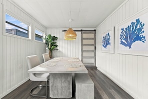 A dining area with a long table, chairs, a hanging light fixture, and framed artwork on the walls. - Walk to Cocoa Beach + Kids Clubhouse+Private Yard (Cocoa Beach)