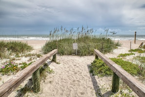 A sandy beach path with wooden railings leading to the ocean, surrounded by vegetation and a warning sign. - Walk to Cocoa Beach + Kids Clubhouse+Private Yard (Cocoa Beach)