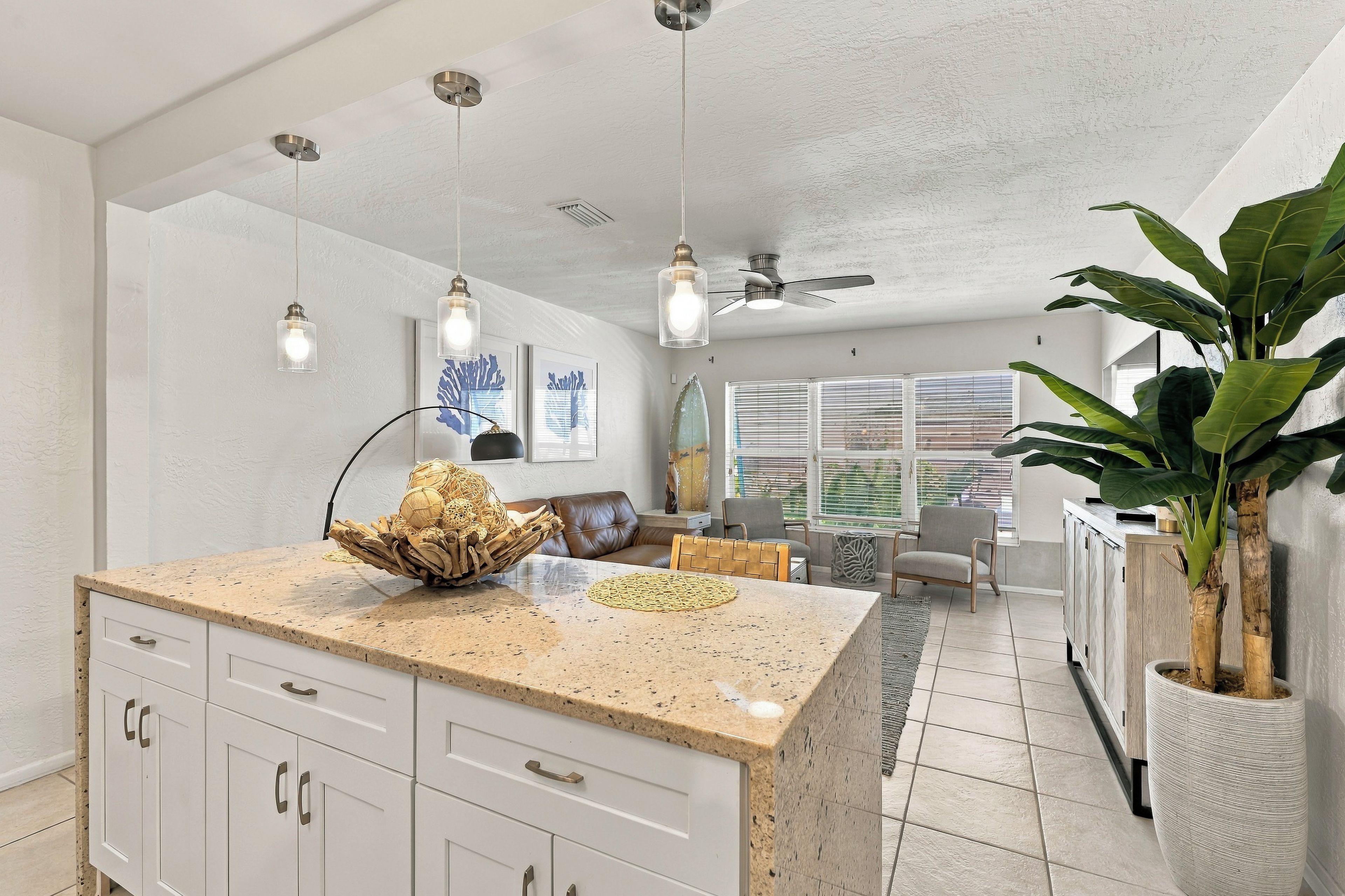 Une cuisine moderne dotée d’un plan de travail en granit, de meubles blancs, de luminaires suspendus et d’un ventilateur de plafond.