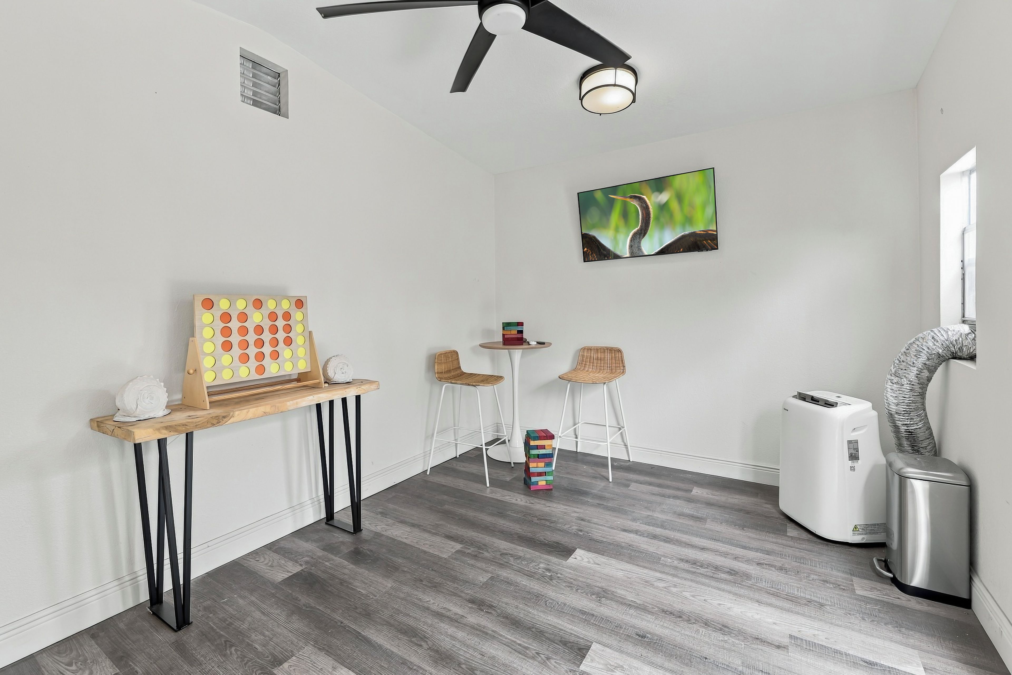 A room with a ceiling fan, a wall-mounted light, a painting, a small table with chairs, and a white air purifier.