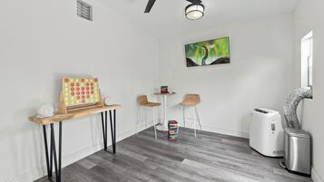 A room with a ceiling fan, a wall-mounted light, a painting, a small table with chairs, and a white air purifier.