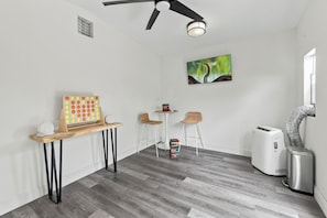 A room with a ceiling fan, a wall-mounted light, a painting, a small table with chairs, and a white air purifier. - Walk to Cocoa Beach + Kids Clubhouse+Private Yard (Cocoa Beach)