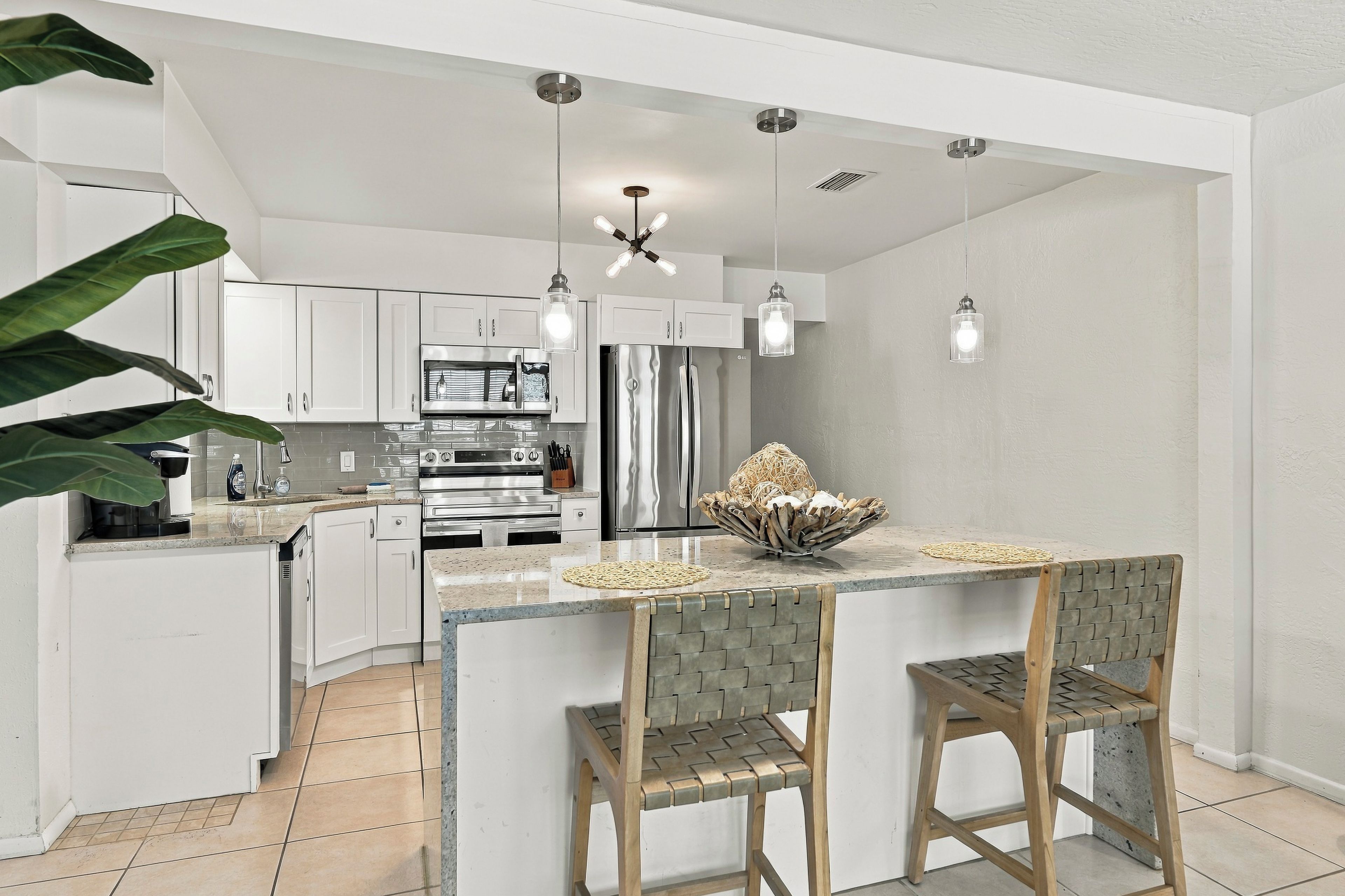 A modern kitchen with white cabinetry, stainless steel appliances, a central island with bar stools, and pendant lighting.