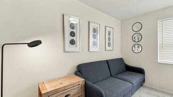 Une pièce avec un canapé gris, une commode en bois et des œuvres d’art encadrées accrochées au mur.