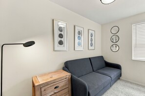 Une pièce avec un canapé gris, une commode en bois et des œuvres d’art encadrées accrochées au mur.