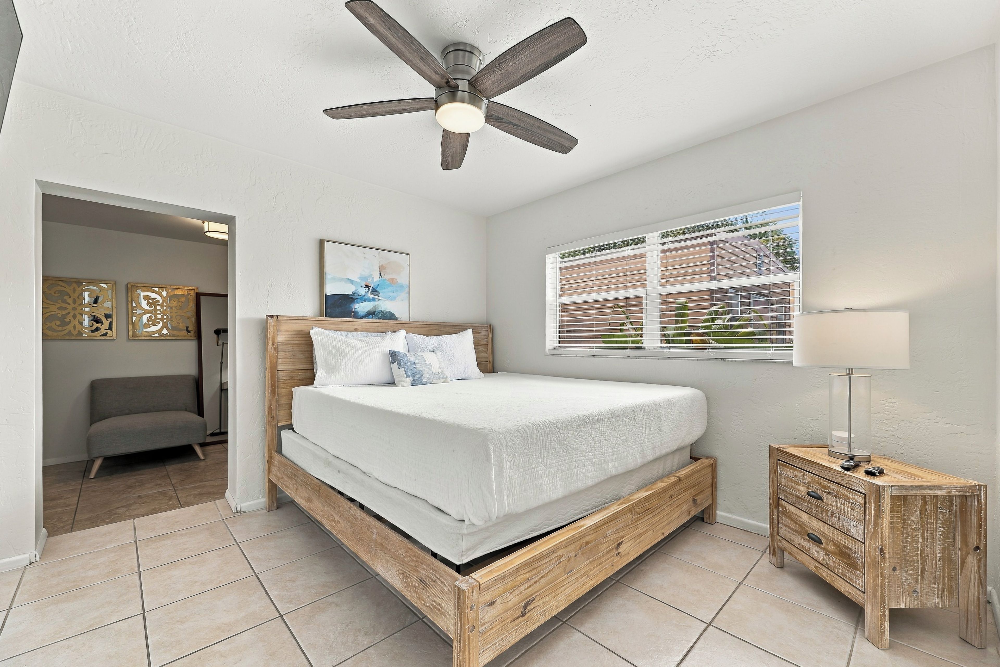 A bedroom with a wooden bed, a ceiling fan, a bedside table, and a window with blinds.