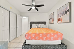 A bedroom with a bed, a ceiling fan, a door, and two paintings on the wall. - Walk to Cocoa Beach + Kids Clubhouse+Private Yard (Cocoa Beach)