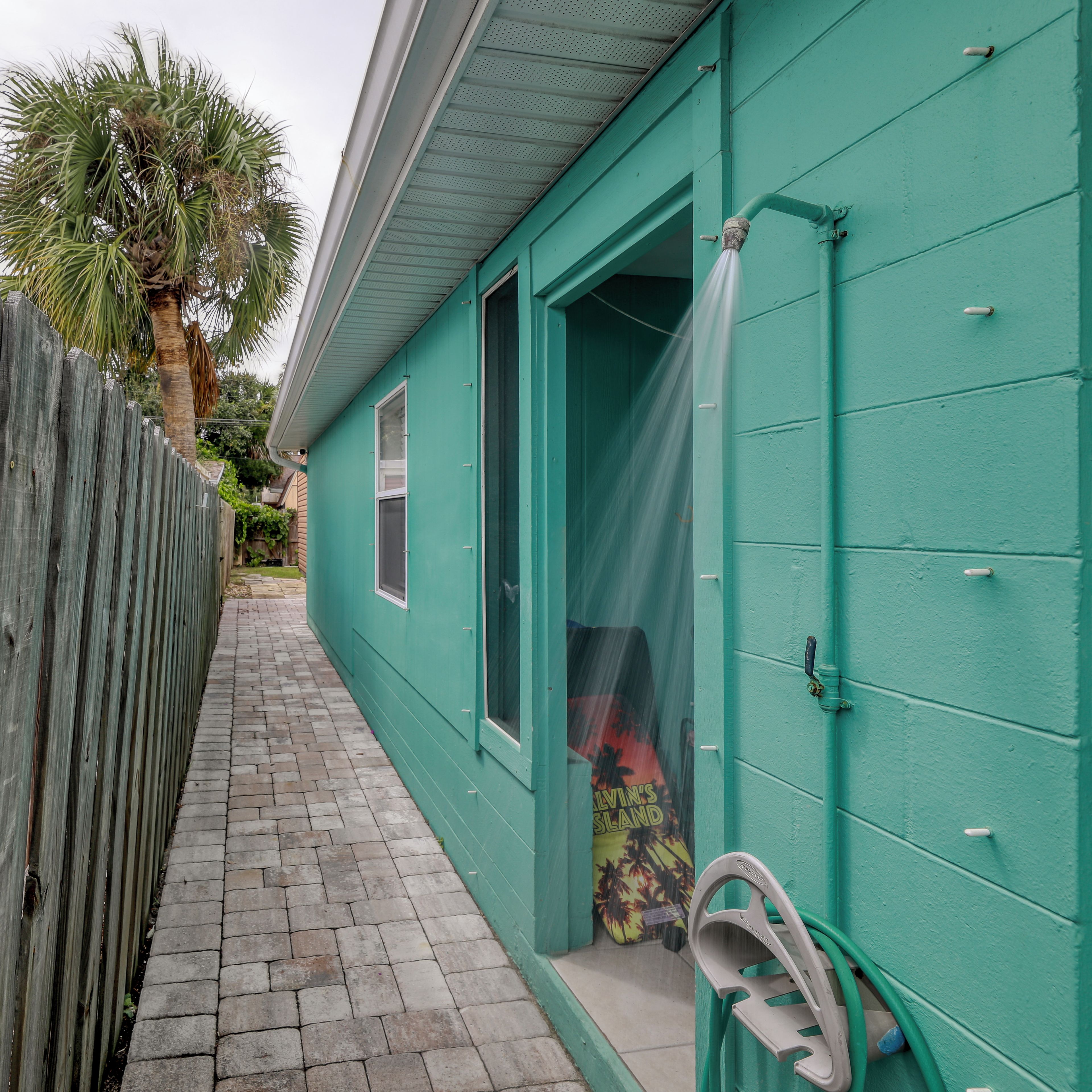 A narrow pathway leading to a teal-colored building with a wooden fence on one side.