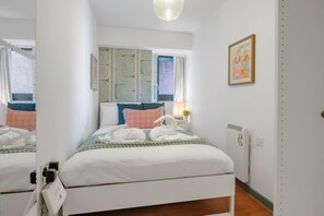 Ein Hotelzimmer mit Bett, Nachttisch mit Lampe, Heizkörper und einem Fenster mit Vorhängen.