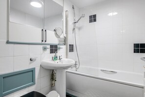 Un baño con lavamanos blanco, espejo y ducha con cabezal de ducha de mano.