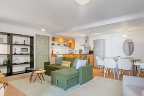 Ein modernes Wohnzimmer mit einem grünen Sofa, einem Essbereich mit weißen Stühlen und einer Küche mit Holzschränken.