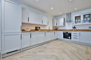 A modern kitchen with white cabinetry, a wooden countertop, and a herringbone-patterned floor. - Central 4-Bed Apartment on Mumbles Road (Swansea)