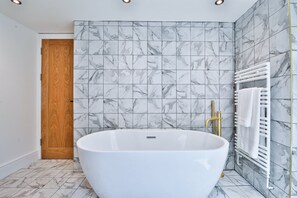 A modern bathroom with a freestanding bathtub, marble tiles, and a wooden door. - Central 4-Bed Apartment on Mumbles Road (Swansea)