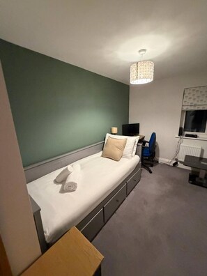 Ein Schlafzimmer mit einem Bett, einem Schreibtisch, einem Stuhl, einer Lampe und einem Fenster.