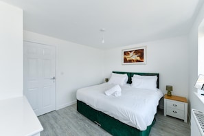 A hotel room with a bed, a nightstand, a lamp, a painting on the wall, and a white door. - Modern 2-Bed Home w/ EV Charger & Garden (Nottingham)