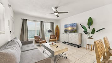 A living room with a sofa, chairs, a coffee table, a ceiling fan, a TV, and a cabinet.