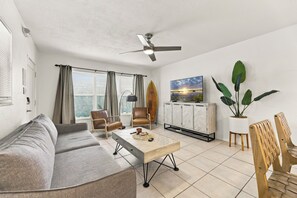 Una sala de estar con sofá, sillas, una mesa de centro, ventilador de techo, televisor y un mueble de almacenamiento.