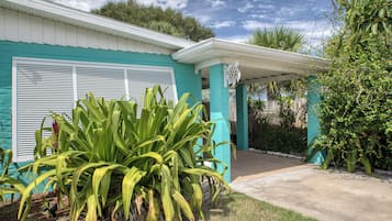 A house with a covered porch, a garage with a shutter, and a garden with large green plants.