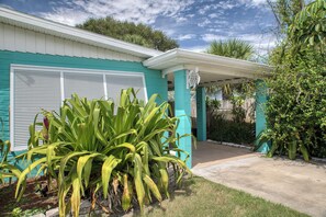 A house with a covered porch, a garage with a shutter, and a garden with large green plants. - Walk to Cocoa Beach & Downtown | 2BR w/ King Bed (Cocoa Beach)