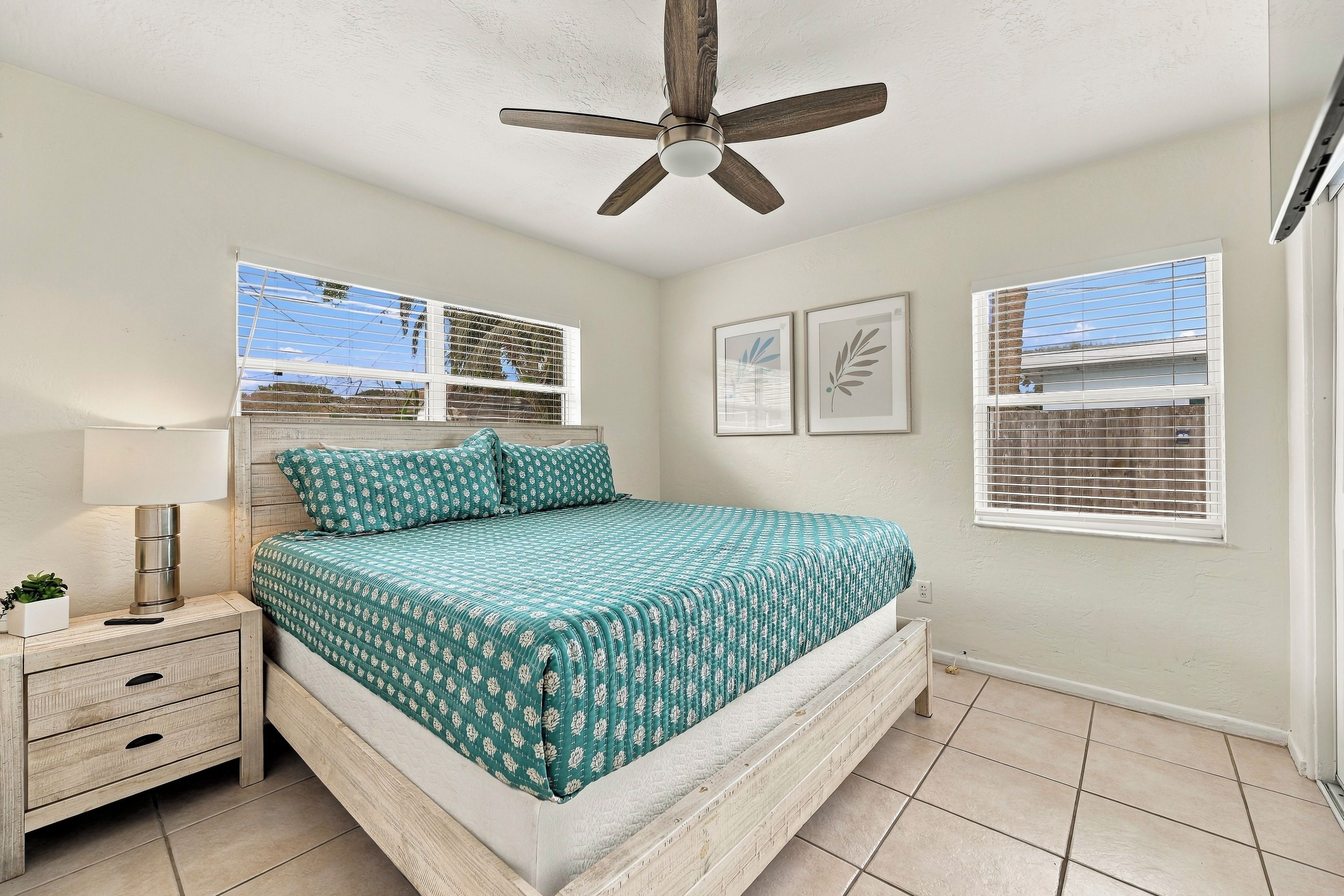 A bedroom with a bed, bedside tables, a ceiling fan, and windows with blinds.