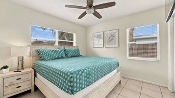A bedroom with a bed, bedside tables, a ceiling fan, and windows with blinds.