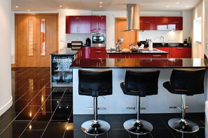 Una cocina moderna con armarios rojos, una campana extractora de acero inoxidable y una isla central con taburetes de bar.