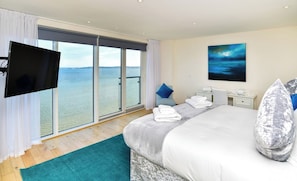 A bedroom with a large bed, a TV, a nightstand, a chair, and a view of the water. - Marina Sky Penthouse 4BR City Views with parking (Swansea)