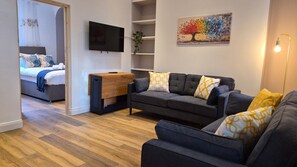 Ein modernes Wohnzimmer mit einer Couch, einem Fernseher, einem Holztisch und einem Bild an der Wand.