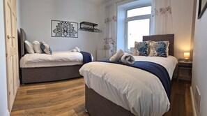 Una camera d'albergo con due letti, pavimento in legno, una finestra con tende e un'opera d'arte appesa al muro.