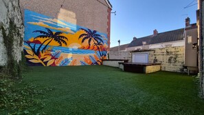 A courtyard with artificial grass, a mural of a beach scene, and a brick wall. - Swansea City & Bay 4-Bedroom House (Swansea)