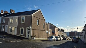 A street with residential buildings, parked cars, and a clear sky. - Swansea City & Bay 4-Bedroom House (Swansea)