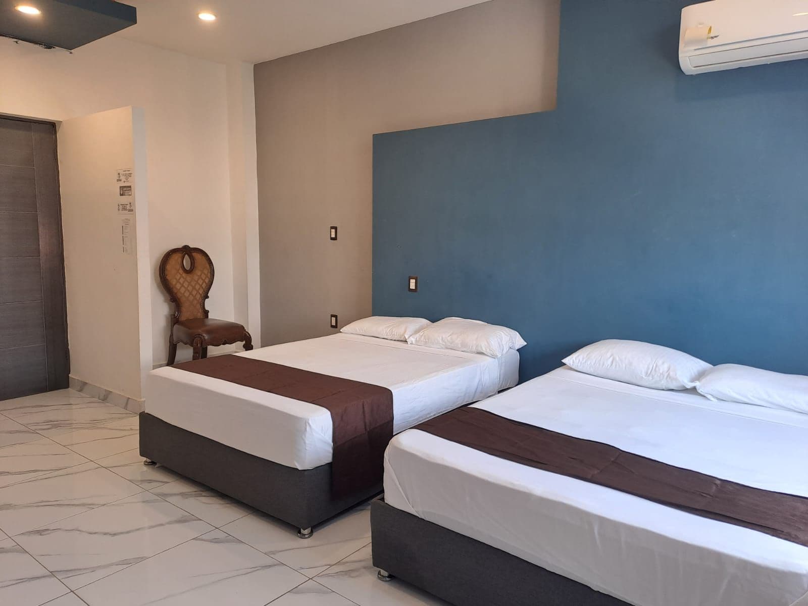 Een hotelkamer met twee bedden, een houten stoel en een blauwe accentmuur.