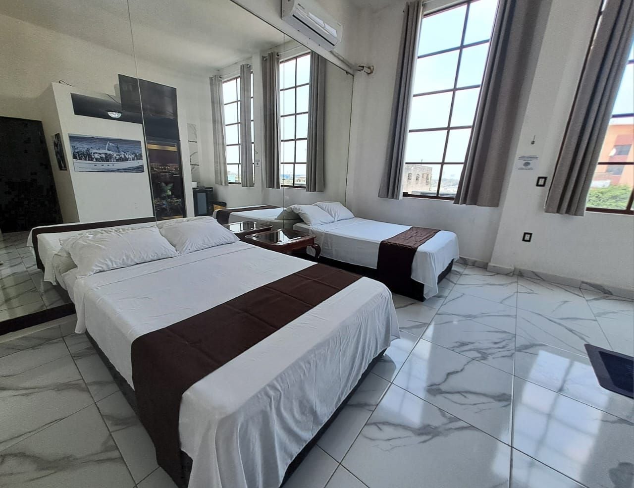 Een hotelkamer met twee bedden, een groot raam en een spiegel.