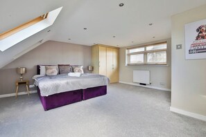 Ein Schlafzimmer mit schräg verlaufender Decke, einem Bett mit violettem Untergestell, einer Stehlampe, einem Heizkörper und einem Poster an der Wand.